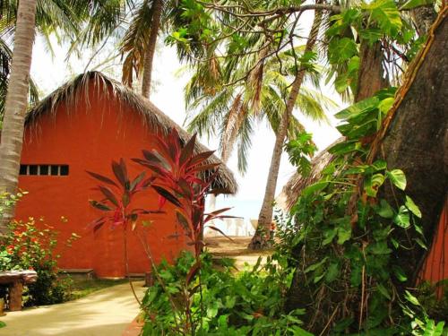 a red building with palm trees in front of it at Pousada Doze Cabanas in Japaratinga