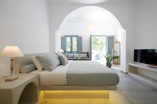 a white bedroom with a bed and a tv at Amara Suites Santorini in Kamari