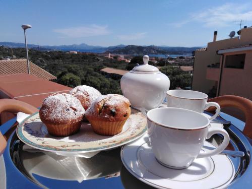 een tafel met muffins en kopjes thee op een balkon bij The Roses Garden in La Maddalena