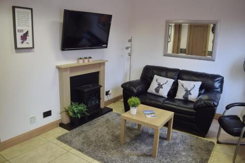 a living room with a black leather couch and a fireplace at Flat 14d Bayhead in Stornoway