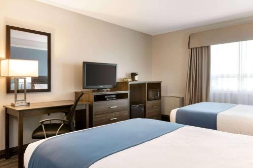 a hotel room with two beds and a desk with a television at Travelodge Suites by Wyndham New Glasgow in New Glasgow