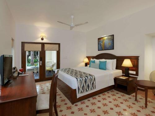 a hotel room with a bed and a desk and a television at Novotel Goa Dona Sylvia Resort in Cavelossim