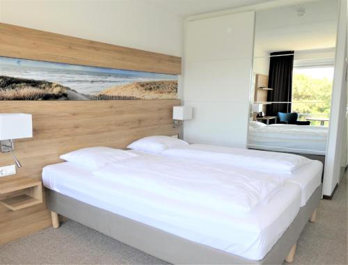 sypialnia z dużym białym łóżkiem z lustrem w obiekcie Strandhotel de Horn w mieście Callantsoog