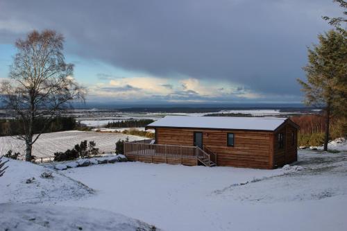 a log cabin in the snow with snow on the ground at Burgie Woodland Lodges in Forres