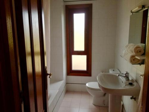 a bathroom with a toilet, sink, tub and window at Hotel Baccus in Carballino