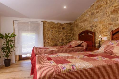 a bedroom with two beds and a stone wall at Casa Brétema en 1ª línea de playa in Boiro