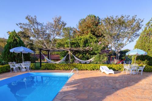 a pool with chairs and umbrellas and a hammock at Pousada Lua Luana in Cambuquira