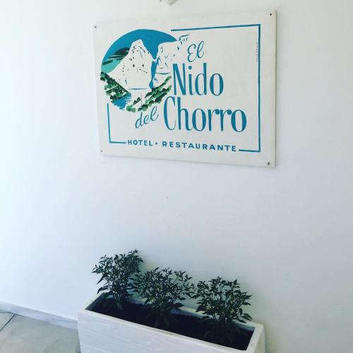a sign on a white wall with two plants at El nido del Chorro in Málaga