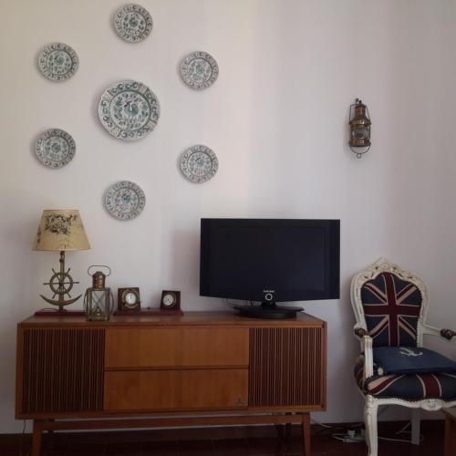 a television on a dresser with a chair and plates on the wall at Elegant and Sea View Excelsior Apartment in Levanto