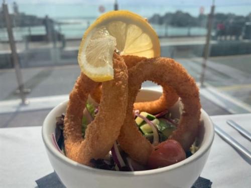 a bowl of food with onion rings and a lemon at The Harbour House Sea front Hotel in Portpatrick