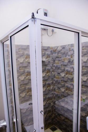 a glass shower door in a bathroom with a stone wall at Homestay Garden Rest Kandy in Kandy