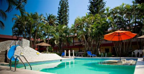 a swimming pool with an umbrella and chairs and trees at Los Andes Coatzacoalcos in Coatzacoalcos