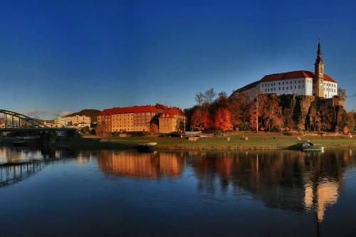 a building on a hill next to a body of water at Krásný byt v centru Děčína in Děčín