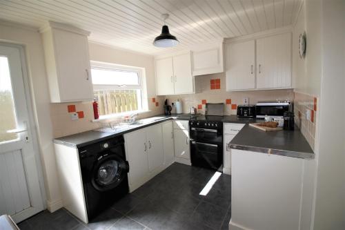 een keuken met witte kasten en een zwarte vaatwasser bij Maggies Cottage in Bushmills