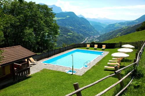 uma piscina com cadeiras, guarda-sóis e montanhas em Berglandhotel Untertheimerhof em Villandro