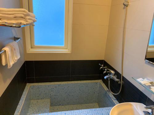 a bathroom with a tub with a window and a sink at Tang Tsai City Hot Spring Hotel in Jiaoxi