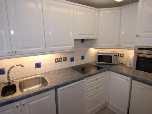a kitchen with white cabinets and a sink and a microwave at Garden View in Kingskerswell
