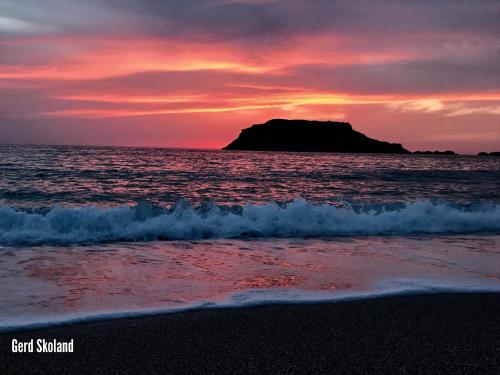 a sunset on the beach with a rock in the ocean at Aegean View Studios in Lefkos Karpathou