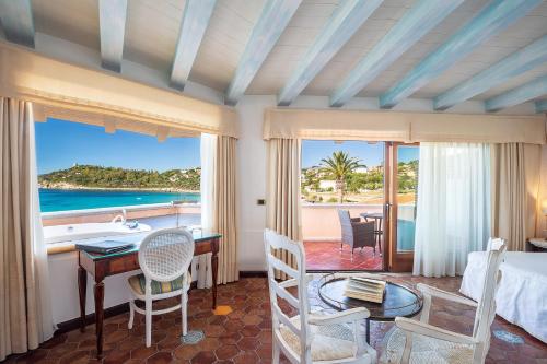 a bedroom with a bed and a desk with a view of the ocean at Hotel La Bitta - Bovis Hotels in Àrbatax