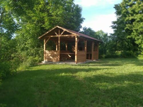 a small wooden pavilion in a field of grass at Dolistówka Apartamenty, pole namiotowe, balia z jacuzzi, ogród warzywny dla gości, plac zabaw dla dzieci in Goniadz