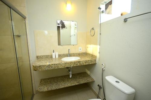 a bathroom with a sink and a toilet and a mirror at Quintal da Arte Suites in Arraial d'Ajuda