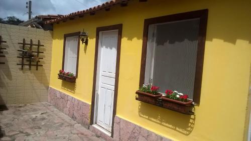 Una casa amarilla con dos ventanas y flores. en O Pouso Condomínio en Mucugê