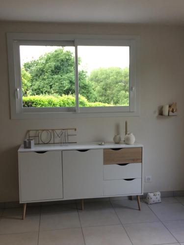 eine weiße Küche mit einem Fenster und einem Tisch in der Unterkunft LE PETIT MONTY Gite Côté Jardin in Saint-Malo-du-Bois
