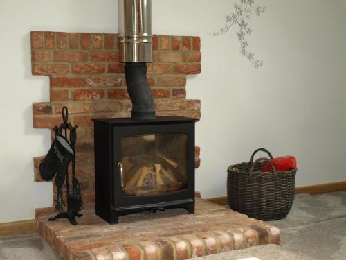 a fireplace with a stove on a brick wall at New Bury Cottage near Goodwood in Chichester