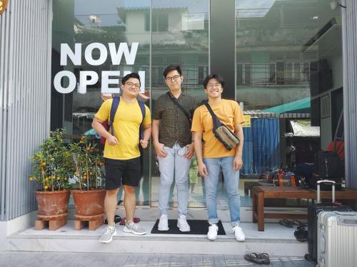 three men standing in front of a now open sign at Rich8 Hostel in Bangkok