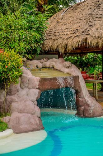 a waterfall in a swimming pool with a straw hut at Camaya-an Paradise Beach Resort in Malabugas