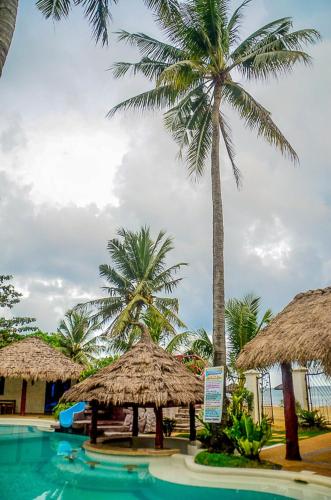 a swimming pool with two straw umbrellas and palm trees at Camaya-an Paradise Beach Resort in Malabugas