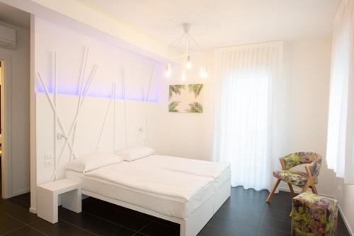 ein weißes Schlafzimmer mit einem Bett und einem Stuhl in der Unterkunft Sunrise Rooms in Grado