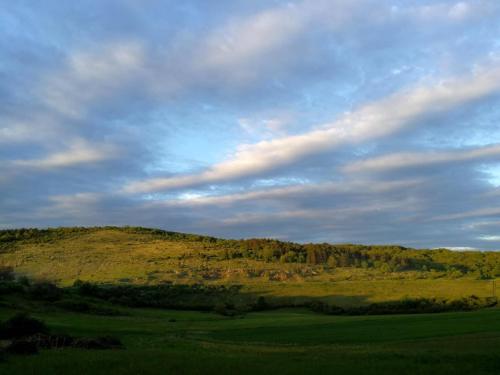 a green field with a hill and a cloudy sky at Panoráma Üdülő in Aggtelek