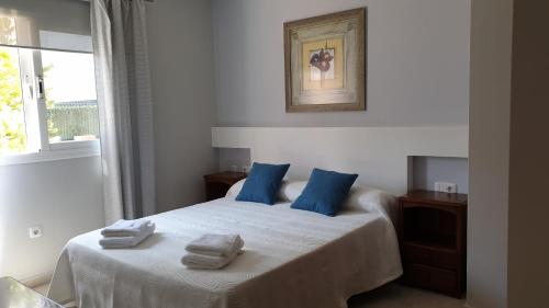Una cama blanca con almohadas azules y toallas. en Sunny & New Apartamento in Caleta de Fuste, en Caleta de Fuste