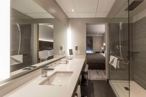 a bathroom with two sinks and a shower and a bed at Hôtel & Suites Normandin Lévis in Lévis