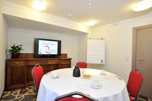a room with a table with red chairs and a tv at Golden Tulip Kassel Hotel Reiss in Kassel