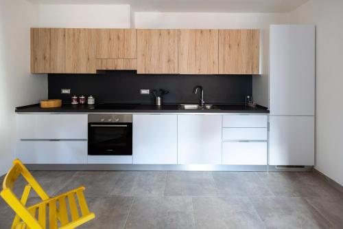 a kitchen with white cabinets and a sink and a yellow chair at Una Finestra sul Lago in Molveno