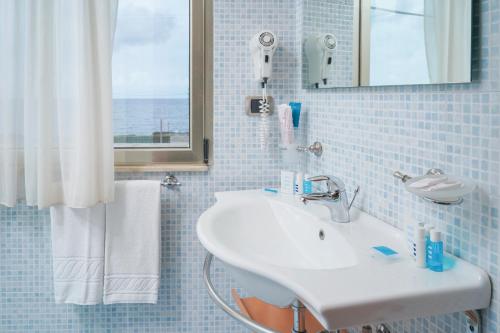 un bagno piastrellato blu con lavandino e finestra di Piccadilly Rooms Restaurant and Beach a Santa Maria al Bagno