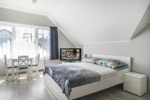 a white bedroom with a bed and a dining table at Niebieska Willa in Jastarnia