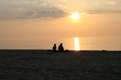 two people sitting on the beach watching the sunset at Baltic Apartments in Pobierowo