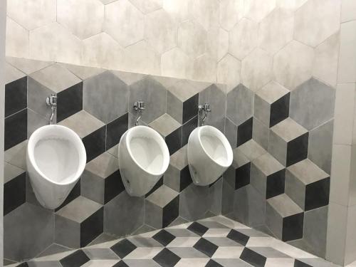 drie urinoirs in een badkamer met zwarte en witte tegels bij Shakti Capsule Hotel Jakarta in Jakarta