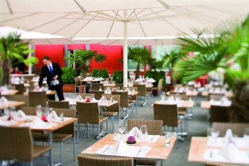 a restaurant with tables and chairs with a person walking in the background at Mövenpick Hotel Zurich Airport in Glattbrugg