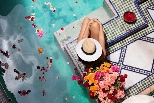 Eine Frau mit einem Hut in einem Pool mit Blumen in der Unterkunft Riad Tamarrakecht in Marrakesch