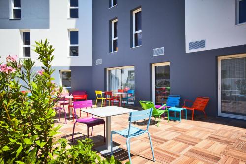 a patio with colorful chairs and a table in front of a building at Hôtel Confort La Rochelle Centre les Minimes in La Rochelle
