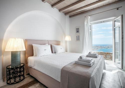 a white bedroom with a bed and a large window at Diana Villa Mykonos in Agios Ioannis Mykonos