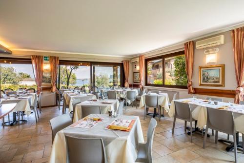 a restaurant with white tables and chairs and windows at Onda Blu Resort in Manerba del Garda