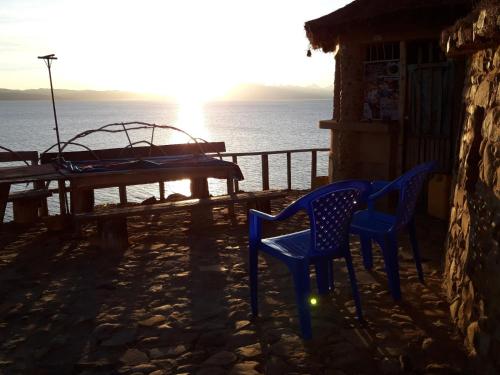 two blue chairs and a table on a patio with the ocean at Hostal Qhana Pacha in Isla de la Luna