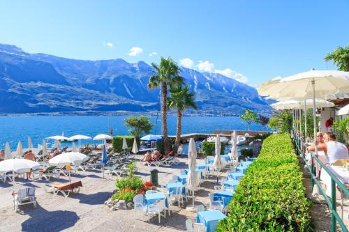 a beach with chairs and umbrellas and a body of water at Hotel San Pietro in Limone sul Garda