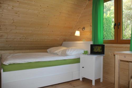 Cama en habitación de madera con escritorio y ordenador portátil en Domki pod lasem blisko morza, en Sztutowo