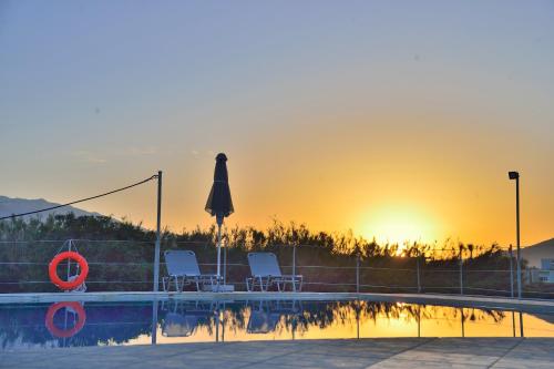 uma piscina com cadeiras e um guarda-sol e o pôr-do-sol em Reina Apartments em Georgioupolis